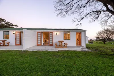 a white house with a picnic table in the yard at Honeyrock Cottages in Kleinmond