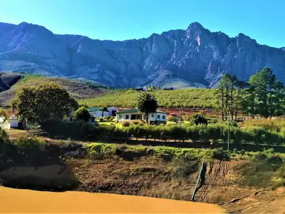 a house in a field with mountains in the background at Vredehoek Guest Farm in Breerivier