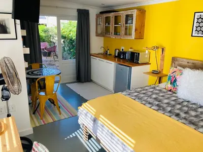 a yellow room with a bed and a kitchen at Modern studio apartment in Cape Town