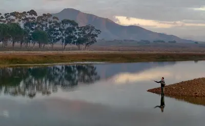 a man standing in the middle of a river fishing at Heron House at Bartholomeus Klip in Hermon