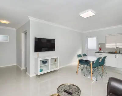 a white living room with a table and a tv at Ocean Way Villas - Self Catering in Cape Town