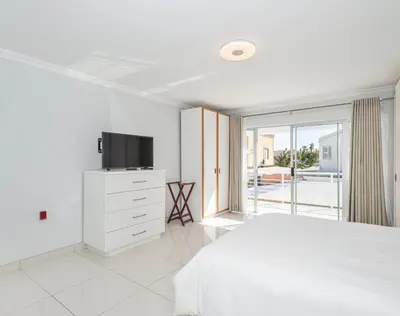 a white bedroom with a bed and a television at Ocean Way Villas - Self Catering in Cape Town