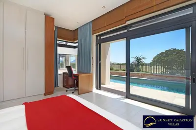 a bedroom with a bed and a large window with a pool at Kite Surfers Beach Villa in Cape Town