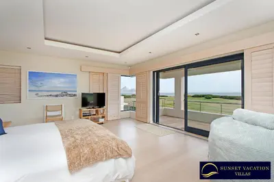 a bedroom with a bed and a balcony with a tv at Kite Surfers Beach Villa in Cape Town