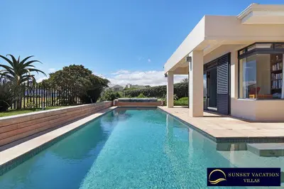a swimming pool in front of a house at Kite Surfers Beach Villa in Cape Town