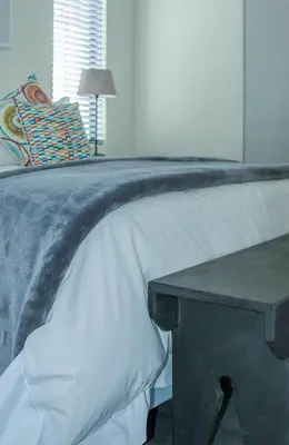 a bed with a gray and white blanket and a table at The Yacht in Hermanus
