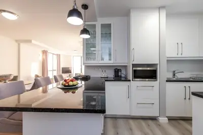 a kitchen with white cabinets and a table with a bowl of fruit at Hibernian Towers 807, Beach Road, Strand in Strand