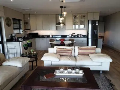 a living room with a white couch and a kitchen at Vrede Selfcatering in Somerset West