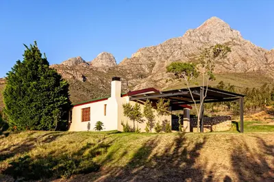 a small white house with mountains in the background at Vergenoegd in Brandwacht