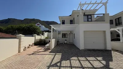 a white house with a garage on a brick driveway at Onrus Holiday Home on Private Estate with Pool in Hermanus