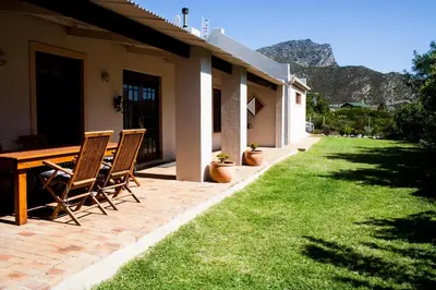 a patio with a table and chairs on a lawn at Hilton House in Pringle Bay