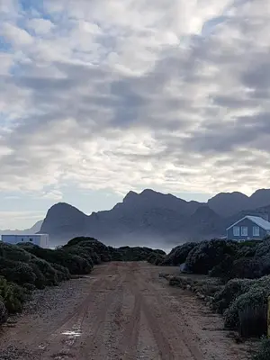 a dirt road with a house and mountains in the background at Kleinblom in Pringle in Pringle Bay