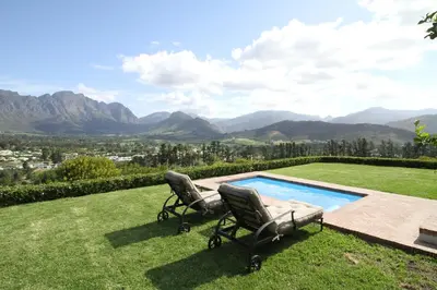 two chairs sitting on the grass next to a swimming pool at The Vineyard Cottage by L' Amitie Estate in Franschhoek