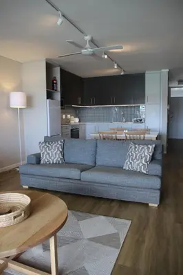 a living room with a blue couch and a kitchen at The Boardwalk Accommodation in Gordonʼs Bay