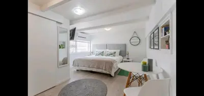a white bedroom with a bed and a table at Antilles on Beach in Cape Town