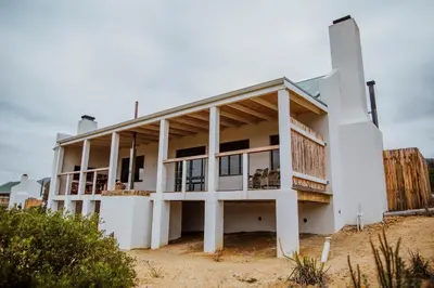a white house on the beach with a fence at Blue Crane Farm Lodge in Botrivier