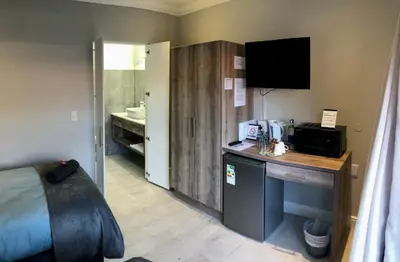 a hotel room with a bed and a desk and a sink at Hermanus Guest Rooms in Hermanus