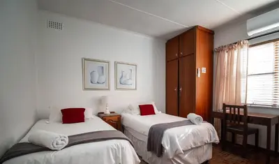 a bedroom with two beds and a desk and a window at Broadway Tygervalley House in Cape Town