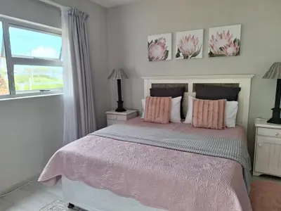 a bedroom with a bed with pink sheets and a window at Silverdunes - GardenView in Bettyʼs Bay