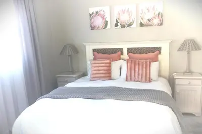 a bedroom with a bed with pink and white pillows at Silverdunes - GardenView in Bettyʼs Bay