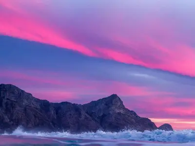 a sunset over the ocean with mountains in the background at PitStop Lodge in Gordonʼs Bay