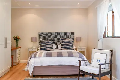 a bedroom with a bed and a chair at Penguino Guesthouse in Hermanus