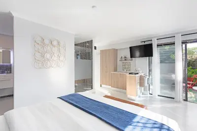 a white bedroom with a bed and a kitchen at Blouberg Studio Apartment in Bloubergstrand