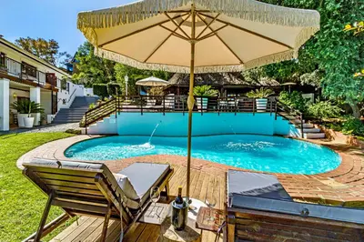a pool with an umbrella and chairs and a table at Villa Helderberg in Somerset West