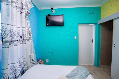 a room with a bed and a tv on the wall at Relaxing Guest House in th Heart of Ndabeni in Cape Town