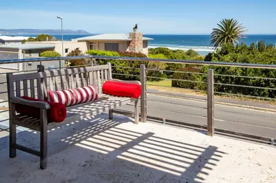a bench with two pillows sitting on a balcony overlooking the ocean at Splendour Hermanus in Hermanus