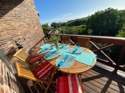 a wooden table on a balcony with a view of the ocean at Hemel in Hermanus Three bedroom Home in Hermanus