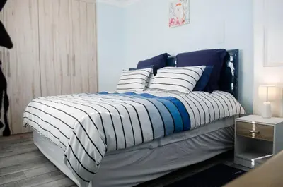 a bed with a blue and white blanket and pillows at Birds Holiday Accommodation 2 in Cape Town