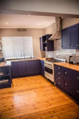 a kitchen with blue cabinets and a wooden floor at Seven on Flora- Hot Tub, Modern with amazing outside area in Hermanus