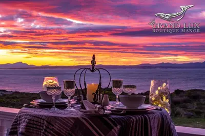 a table with a view of the ocean at sunset at Grand Lux Boutique Manor in Hermanus