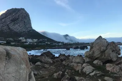 a mountain with rocks in front of a body of water at Rooi Els Sea Cottage in Rooiels
