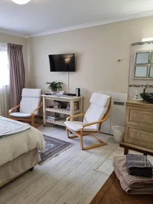 a bedroom with a bed and two chairs and a tv at Barlinka lane Selfcatering flatlet , Somerset West in Cape Town