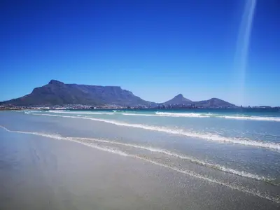 a beach with mountains in the background and the ocean at Cape Town Family Beachfront Apartment Leisure Bay in Cape Town