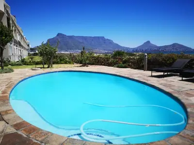 a blue swimming pool with mountains in the background at Cape Town Family Beachfront Apartment Leisure Bay in Cape Town