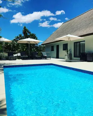 a swimming pool in front of a house with umbrellas at Cape Vermeer in Somerset West