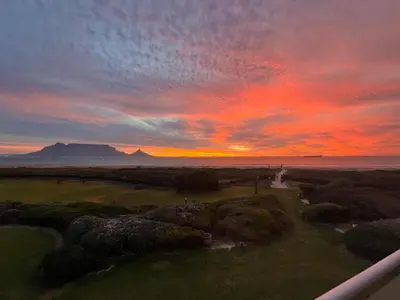 a sunset over a golf course with the ocean at Dolphin Beach Villa E24 direct access to the beach in Cape Town
