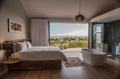 a bedroom with a bed and a tub and a large window at Ridge House in Hermanus