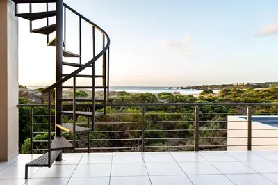 a staircase leading to a balcony with a view of the ocean at Gecko House in Pringle Bay