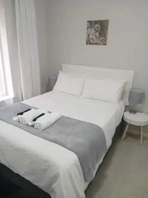 a white bed with two towels on top of it at Jackie’s 3 bedroomed secure beach front apartment Strand Golden Mile in Strand