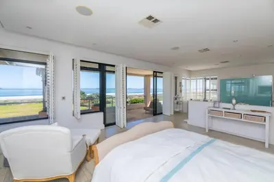 a bedroom with a bed and a sink and windows at Villa Paradis - ocean front with views to behold! in Cape Town
