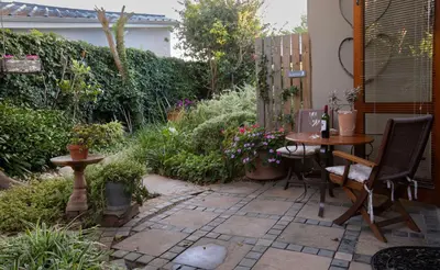 a patio with a table and chairs in a garden at Theebos in Strand