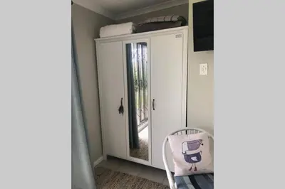 a white cabinet with a mirror and a chair in a room at The West Wing guest suite. Pringle Bay. in Pringle Bay