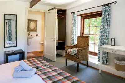 a bedroom with a bed and a chair and a window at Old Potters Inn in Greyton