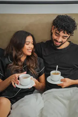 a man and woman sitting on a bed drinking coffee at Bridgewater Apartments by Century City Hotels in Cape Town