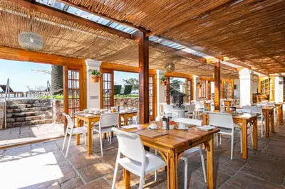 a restaurant with wooden tables and white chairs at Harbour House Hotel - Harbour Square in Hermanus