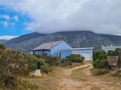 a house on a dirt road with a mountain in the background at Brandys beach house bettys bay in Bettyʼs Bay
